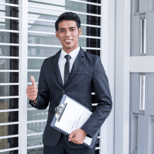 Portrait of a smiling man with short textured hair and a trimmed beard, wearing a dark shirt against a neutral studio background.
