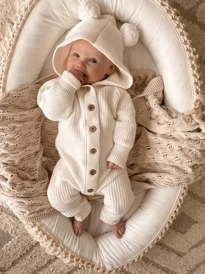 Newborn in a white hooded outfit on an oval cushion