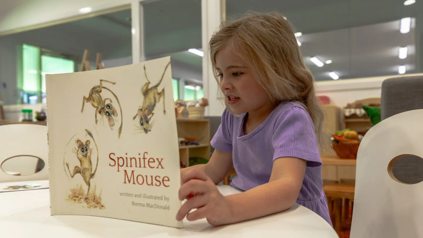 Young girl reading a picture book titled Spinifex Mouse at Kaleidoscope Kids Goodna childcare centre.