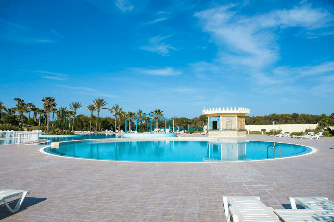 Modern luxury villa with a stone facade, floor-to-ceiling glass windows, and a large outdoor swimming pool with a sun deck and lounge chairs.