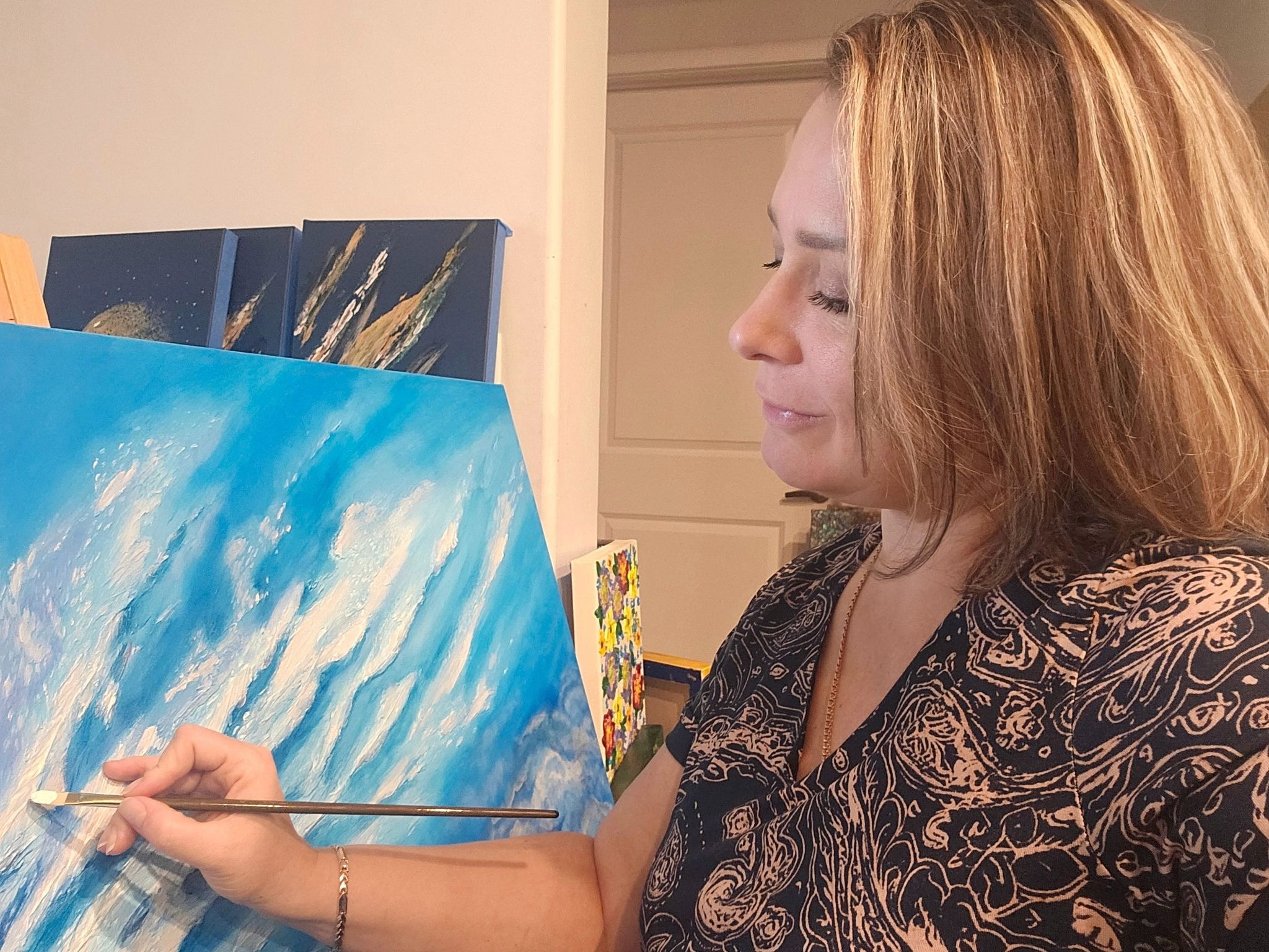 Artist Olha Svieshnikova painting a textured blue abstract artwork in her studio.