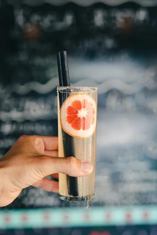 person holding clear drinking glass with brown liquid