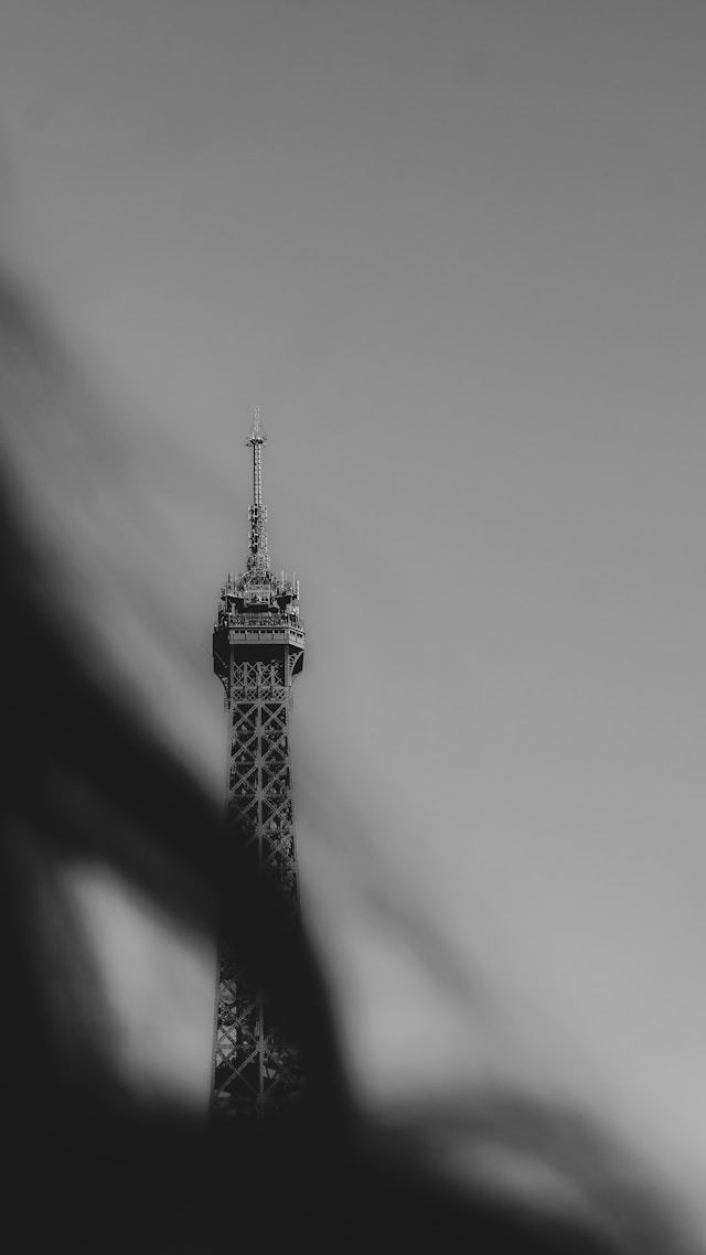 A black-and-white photo capturing the upper section of the Eiffel Tower against a blank sky — minimalist, timeless, and distinctly Parisian.