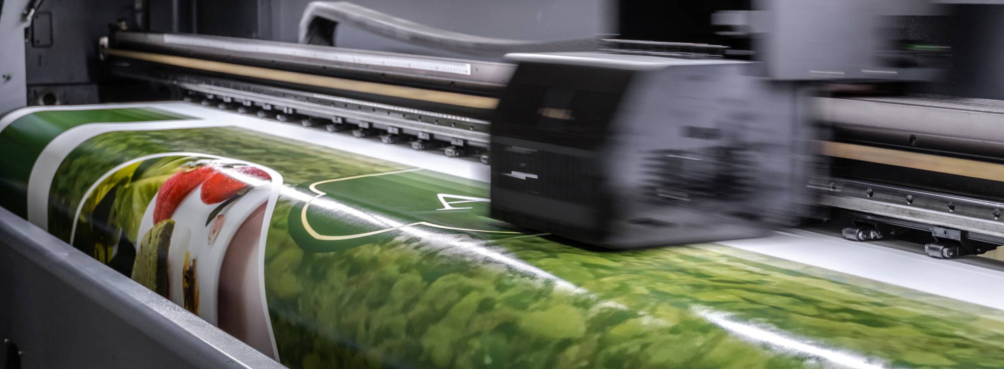 Gros plan sur une imprimante grand format dans l'atelier du Graveur signalétique en Martinique en action, imprimant des graphiques colorés sur du vinyle. La scène traduit l'efficacité industrielle et la technologie.