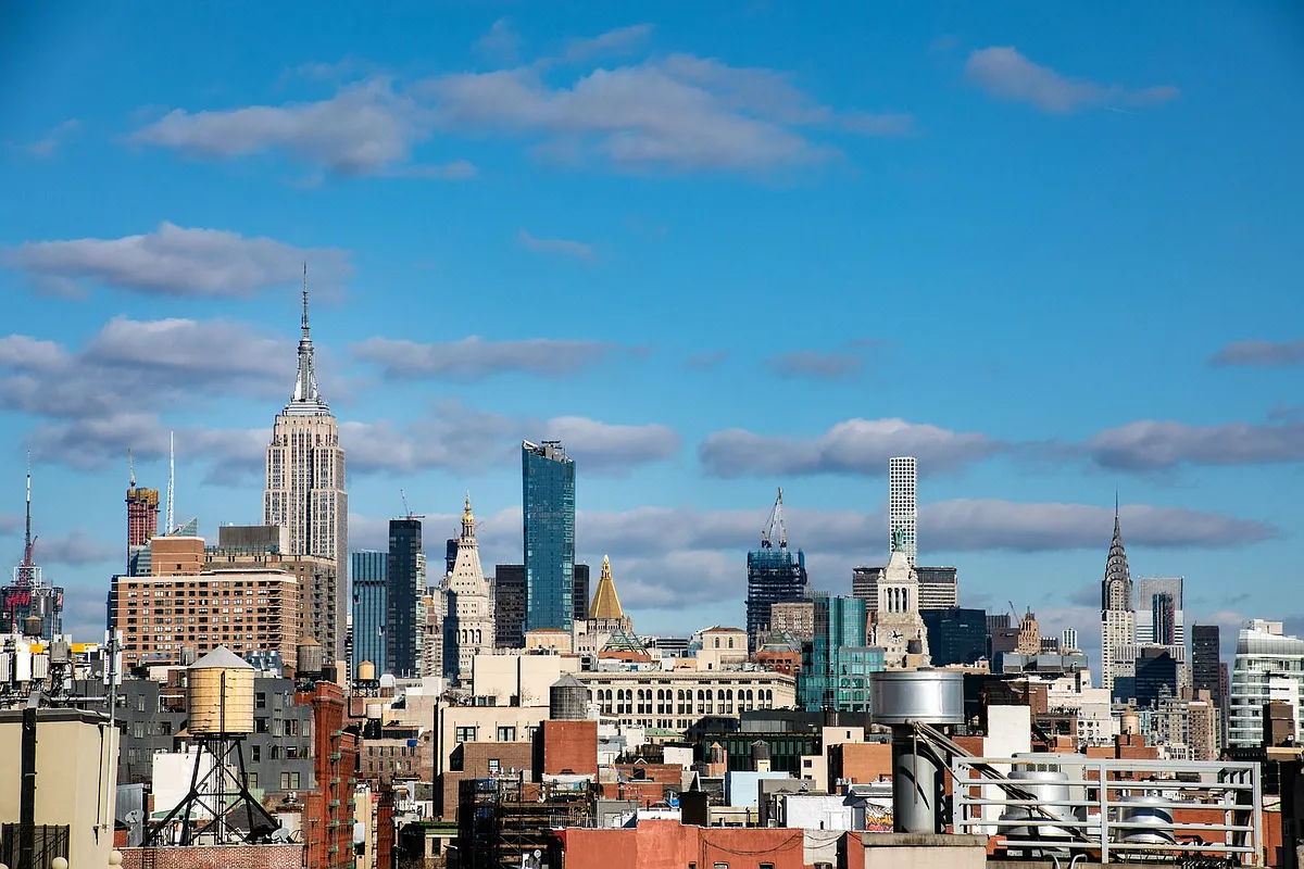 A panoramic view of the New York City skyline from a rooftop, showcasing tall buildings against a clear blue sky.