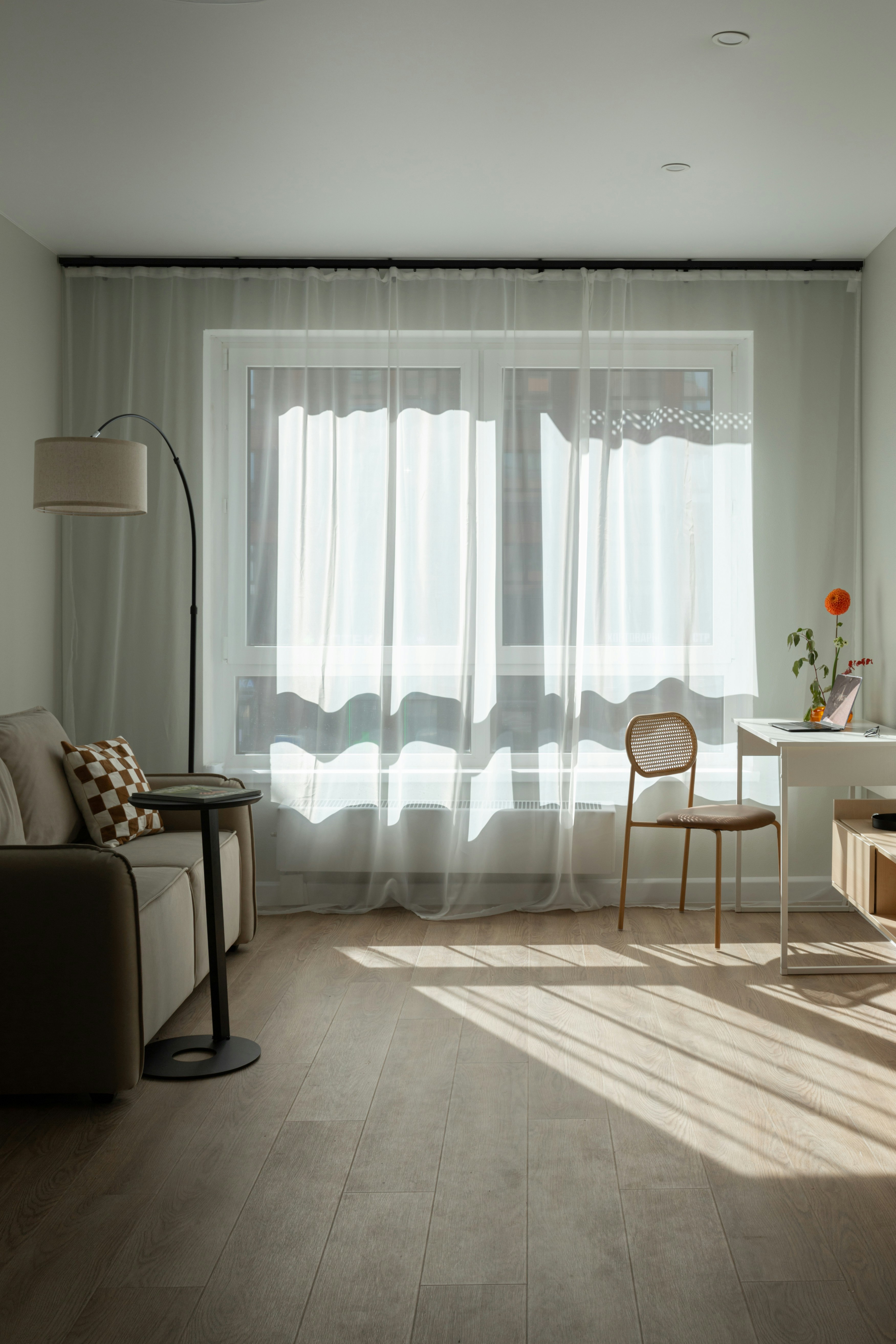 Sunlight streams through sheer curtains onto a living room floor.
