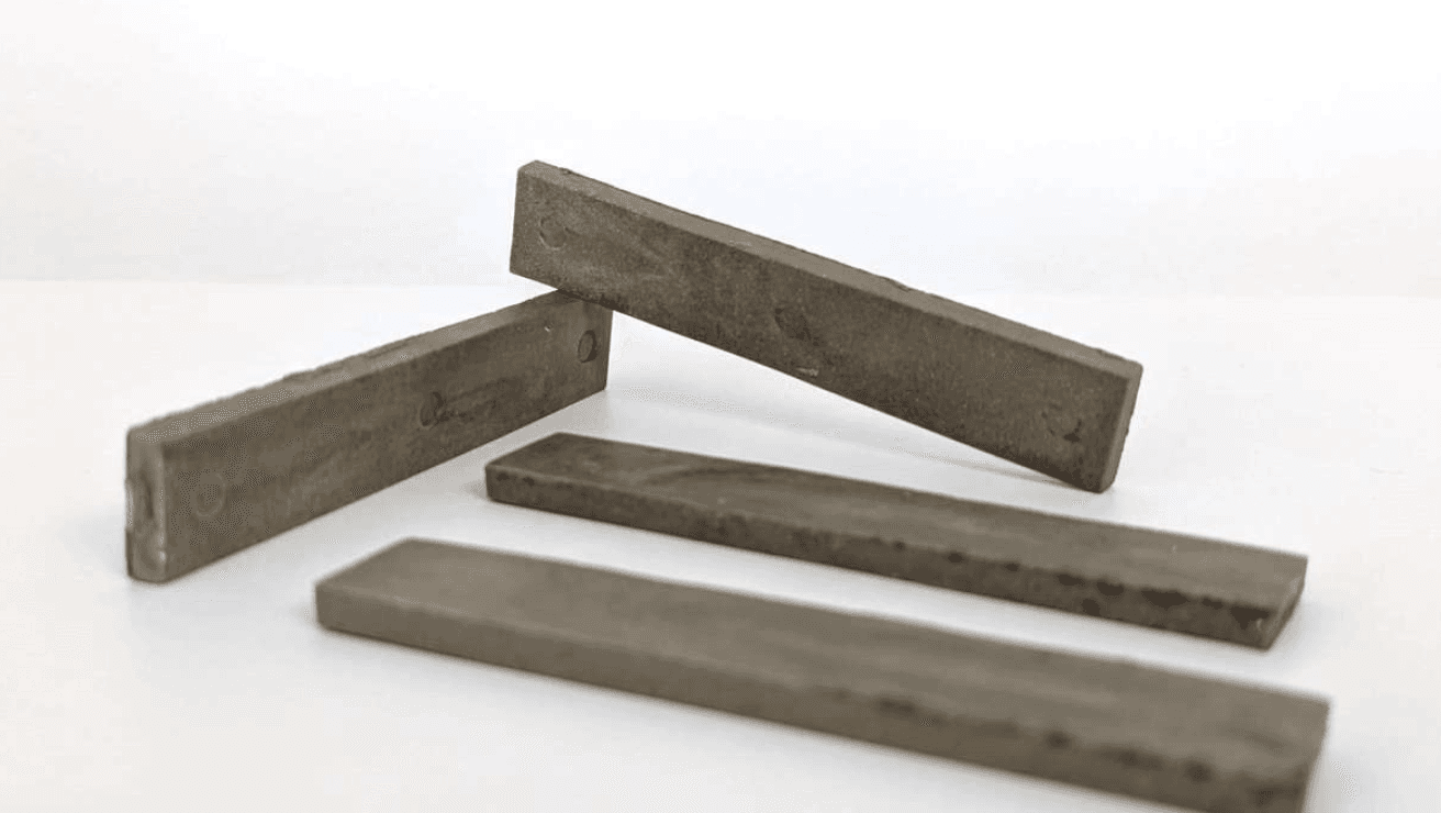 Quatre barreaux rectangulaires en matériau composite gris-brun, disposés en éventail sur fond blanc, utilisés comme éprouvettes de test pour un matériau à base de céramique recyclée