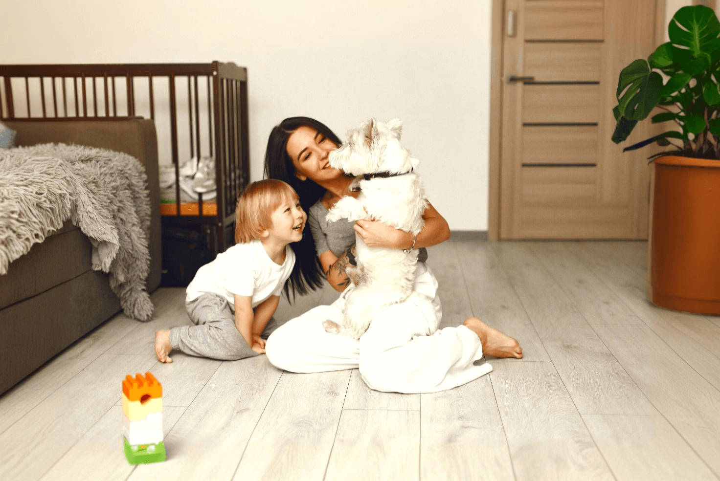 A mother, child, and small dog playing together on light wood-look hybrid flooring, showcasing LUXO Floors’ durable, stain-resistance, and pet-friendly hybrid surface designed for modern family living.