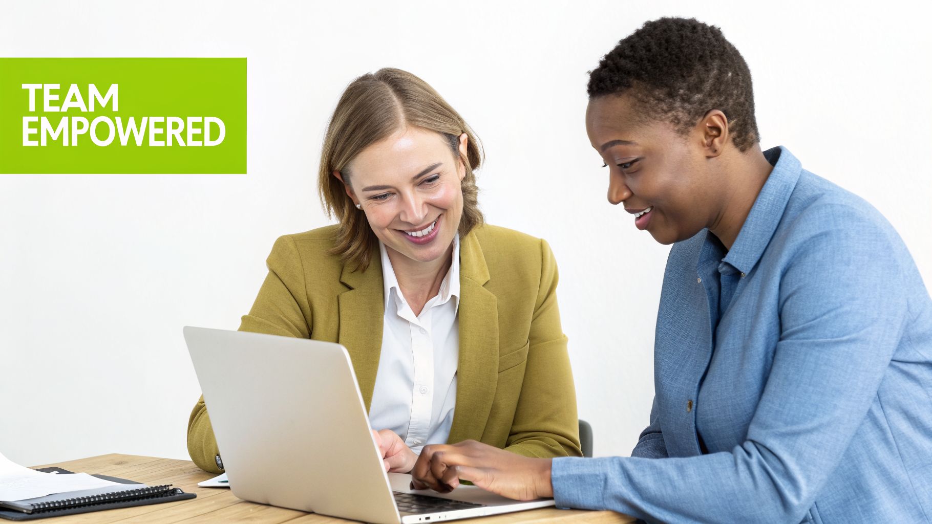 Two diverse women smiling and collaborating, looking at a laptop at a table.