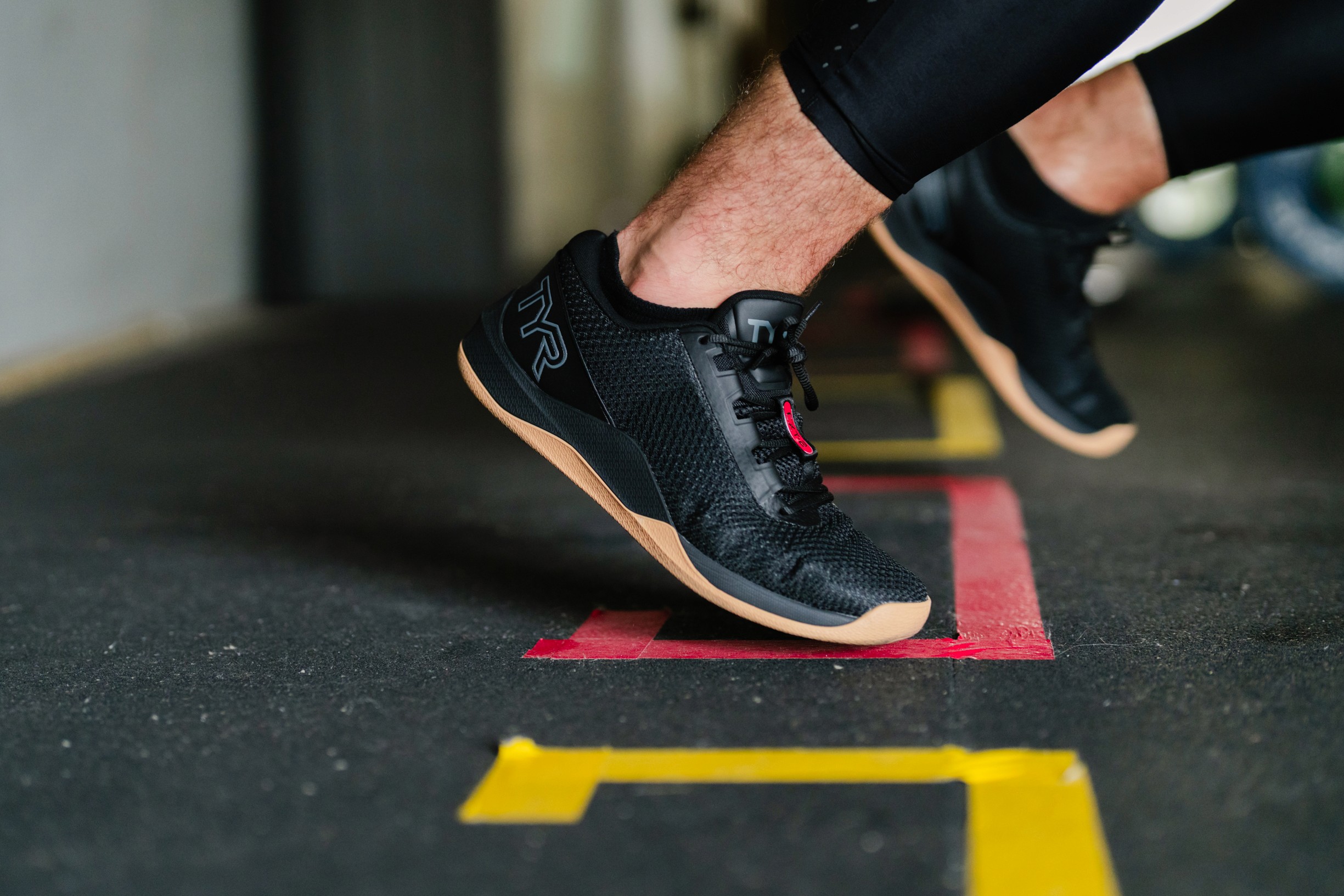 Close-up of a black TYR CXT-2 worn by an athlete standing on a colorful rubber gym mat.