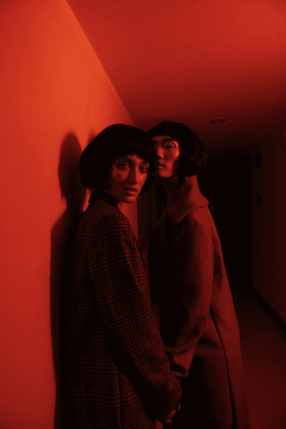 two edgy fashion models wearing long coats standing in a room with red light