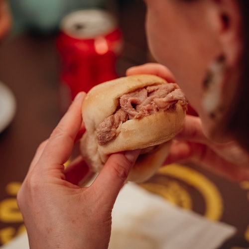 近距离拍摄一个人正拿着并准备吃烤牛肉三明治，背景中模糊的苏打罐可以看到他们的手。