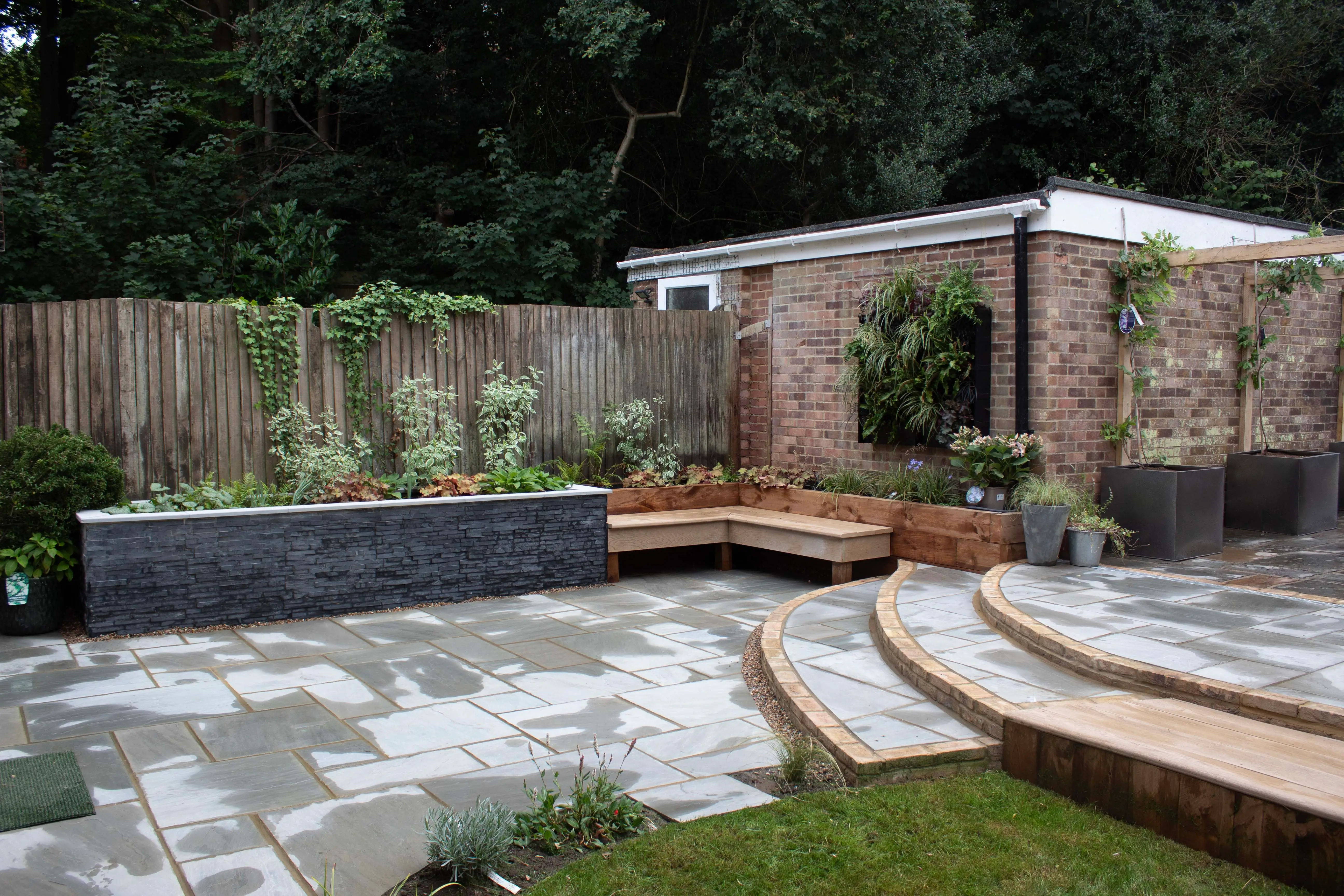 A modern garden featuring a landscaped area with stone pathways, wooden decking, and a serene backdrop of greenery.