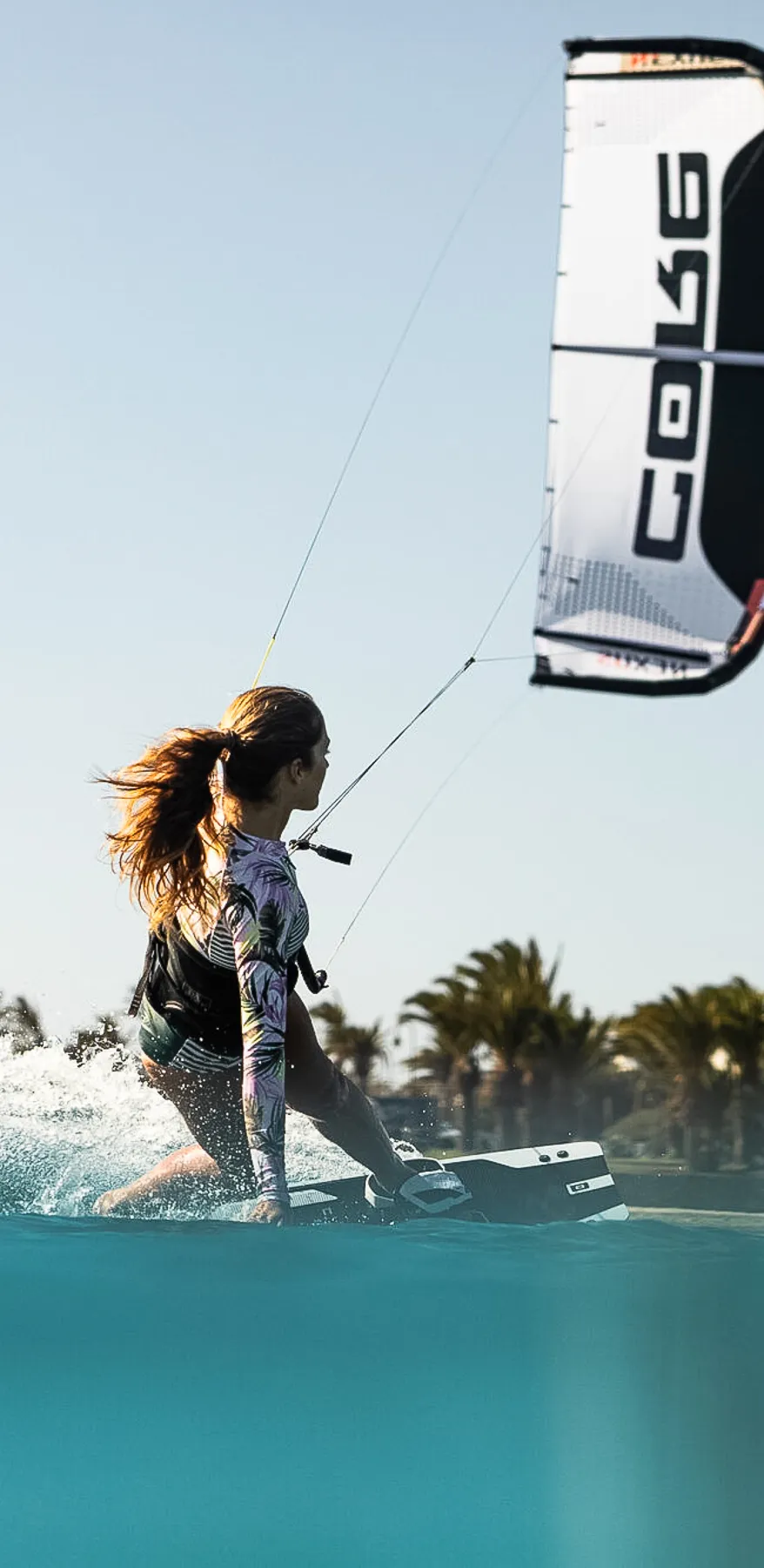 Frau beim Kitesurfen auf türkisfarbenem Wasser in Tarifa an einem sonnigen, windigen Tag