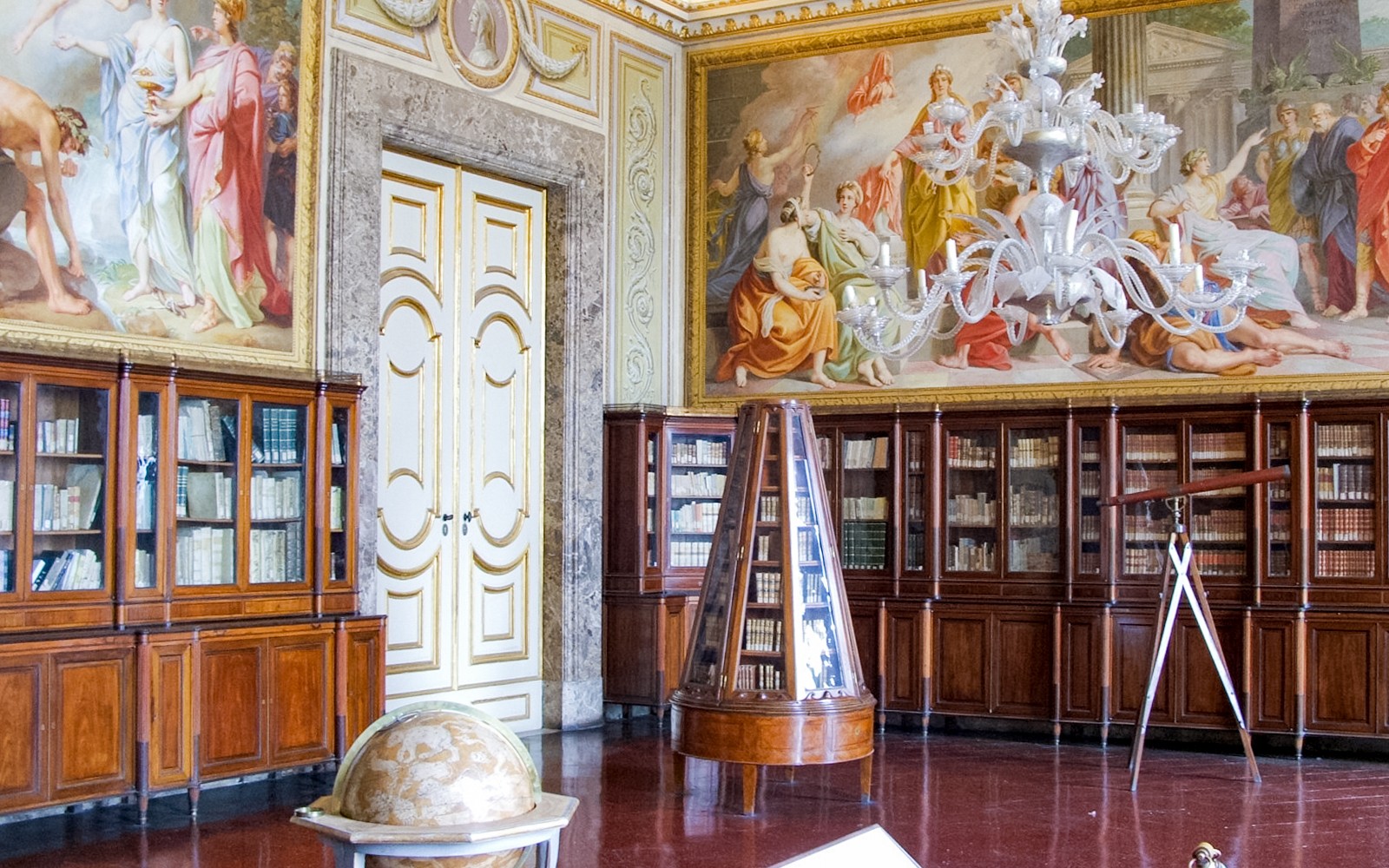 Biblioteca del Palacio Real de Caserta con frescos ornamentados en el techo y estanterías de madera.