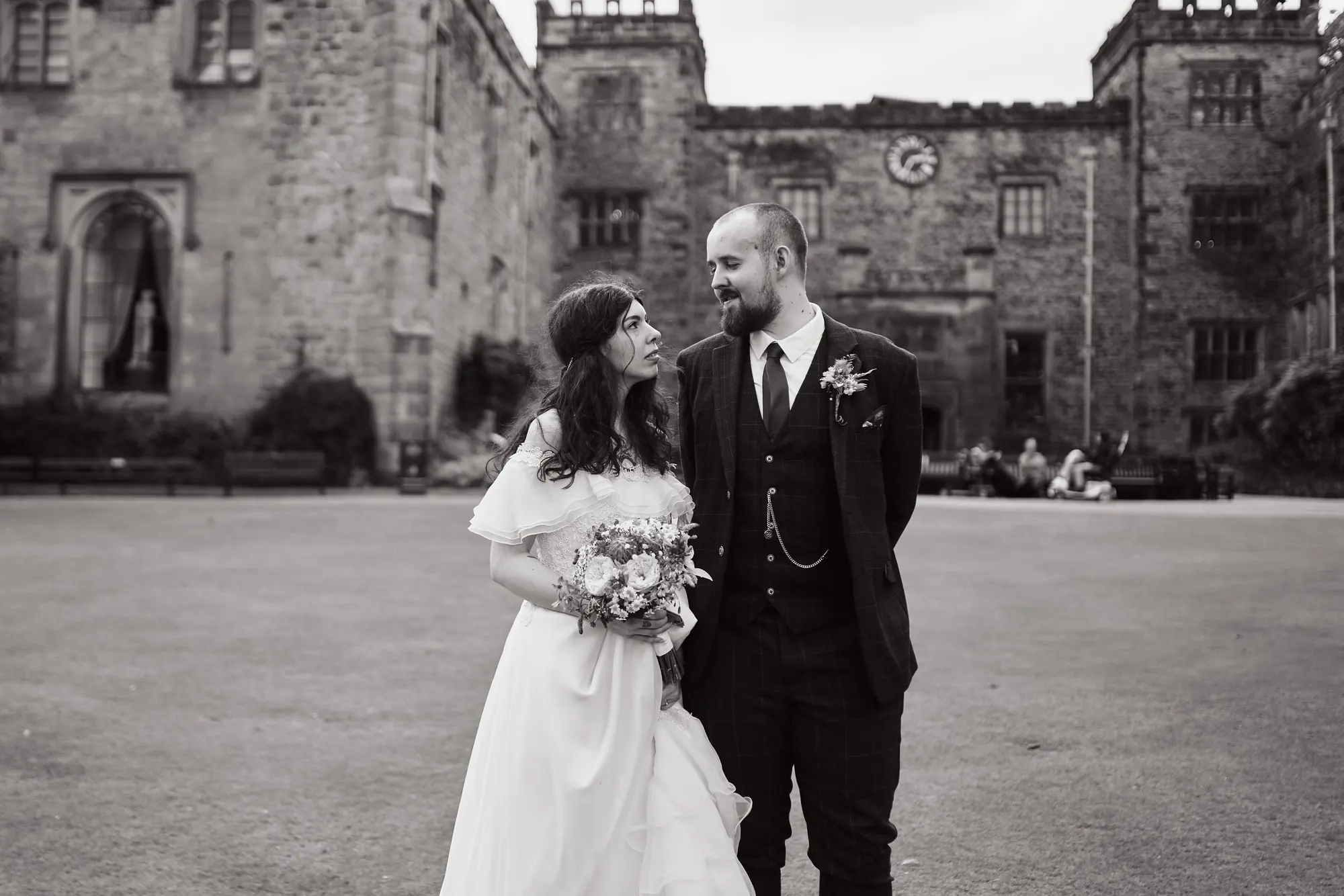 Black and white photo of a bride and groom smiling in the courtyard in front of Towneley Hall’s towers