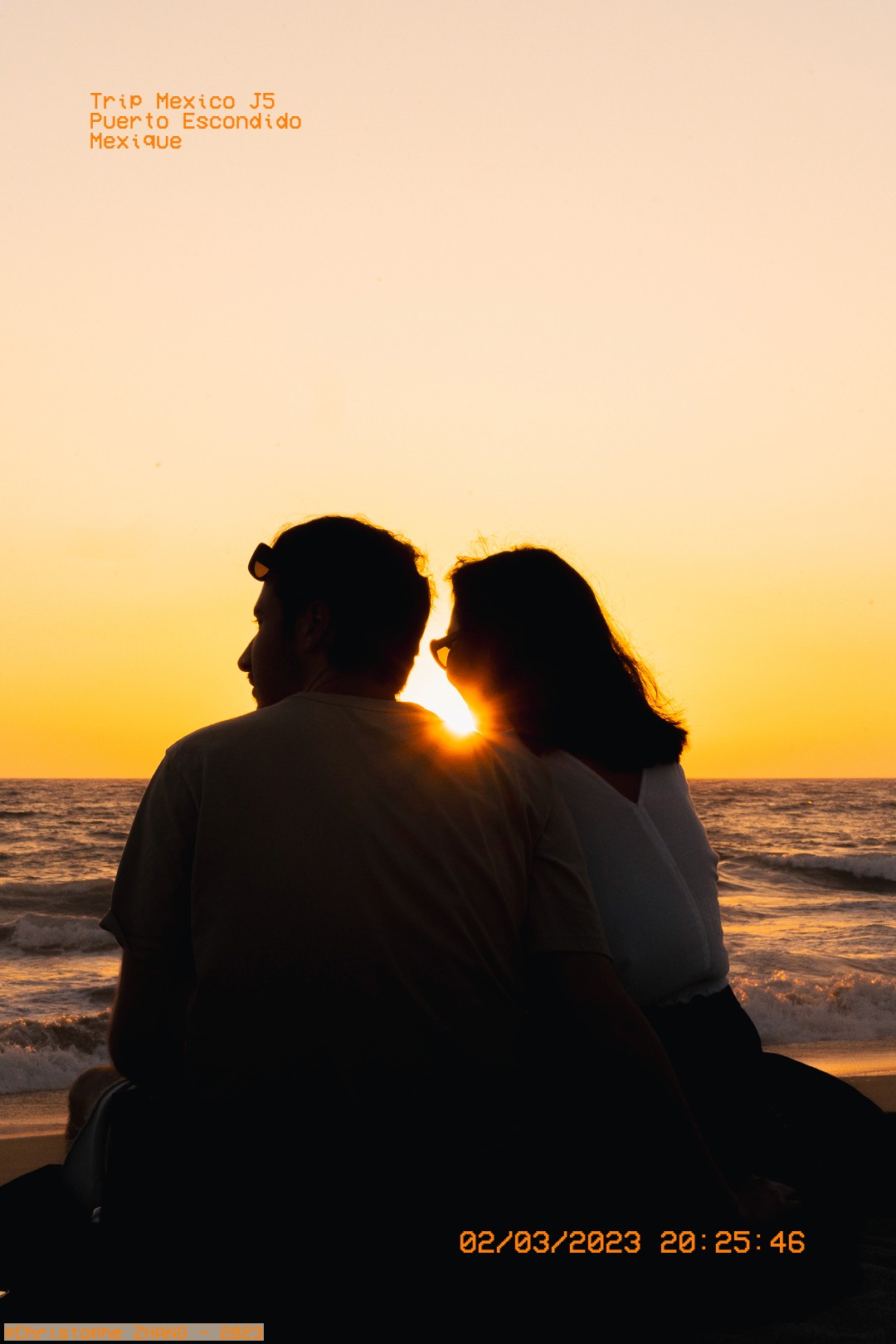 Couple assis sur la plage face au coucher de soleil à Puerto Escondido.