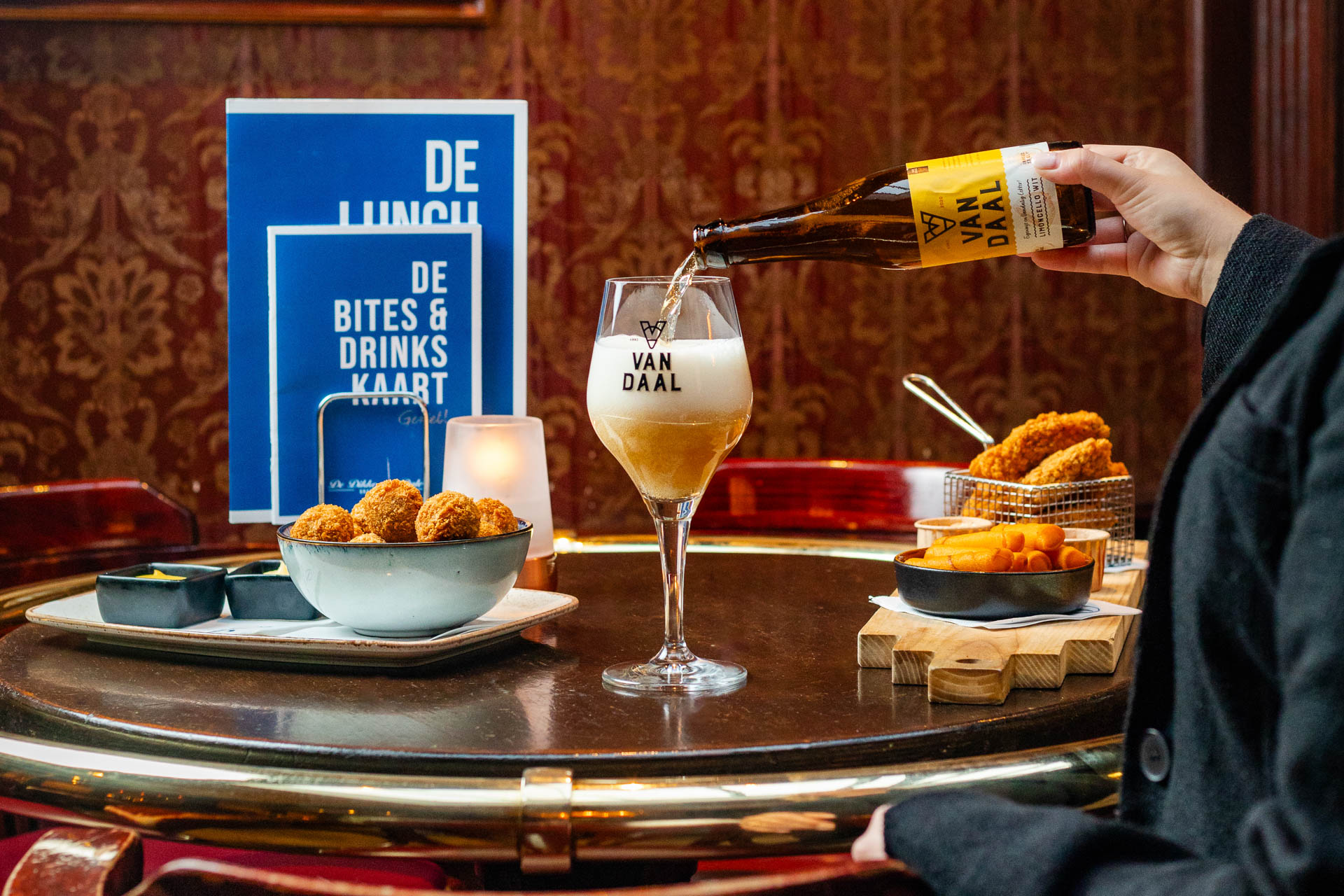 Een tafel bij met de borrel en lunchkaart in beeld en iemand die een biertje inschenkt
