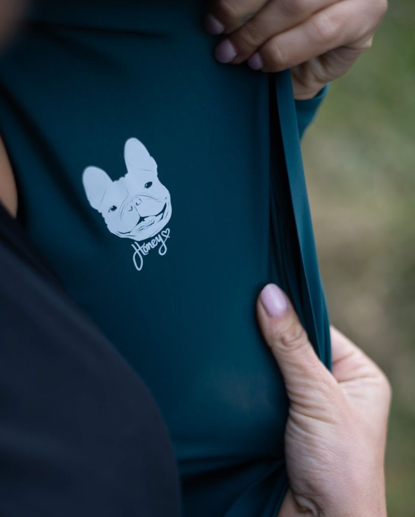 Close-up-of-a-teal-cycling-top- showing-an-inner-graphic-of-a-white-French-Bulldog-head-with-the-handwritten-word-Honey
