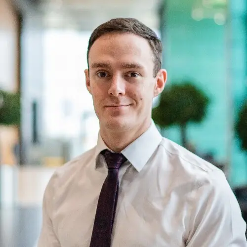 Man in white shirt and purple tie smiles.