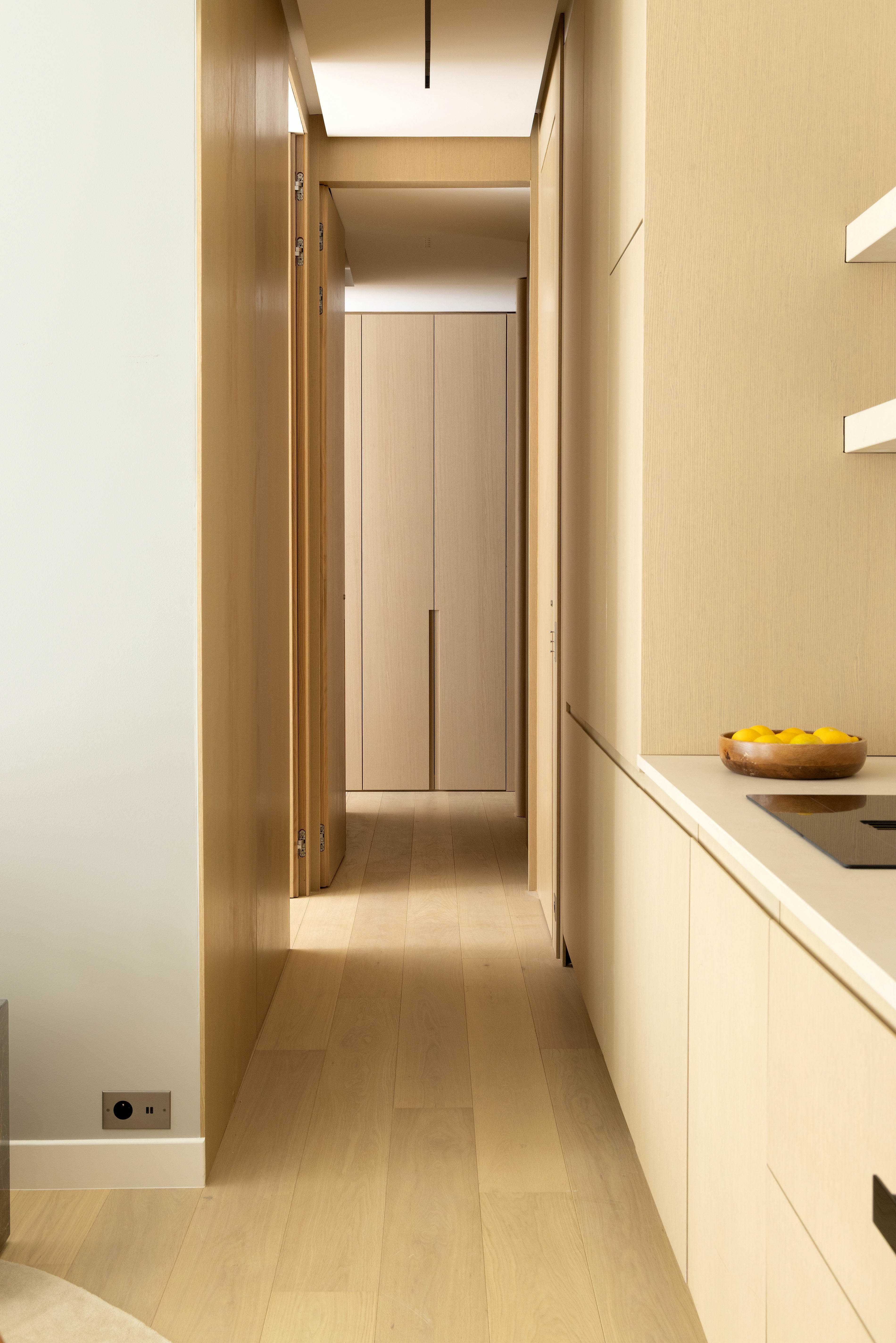 Couloir en bois clair menant aux chambres avec plan de travail cuisine et coupe de citrons