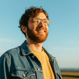 Man in denim jacket smiling outdoors.