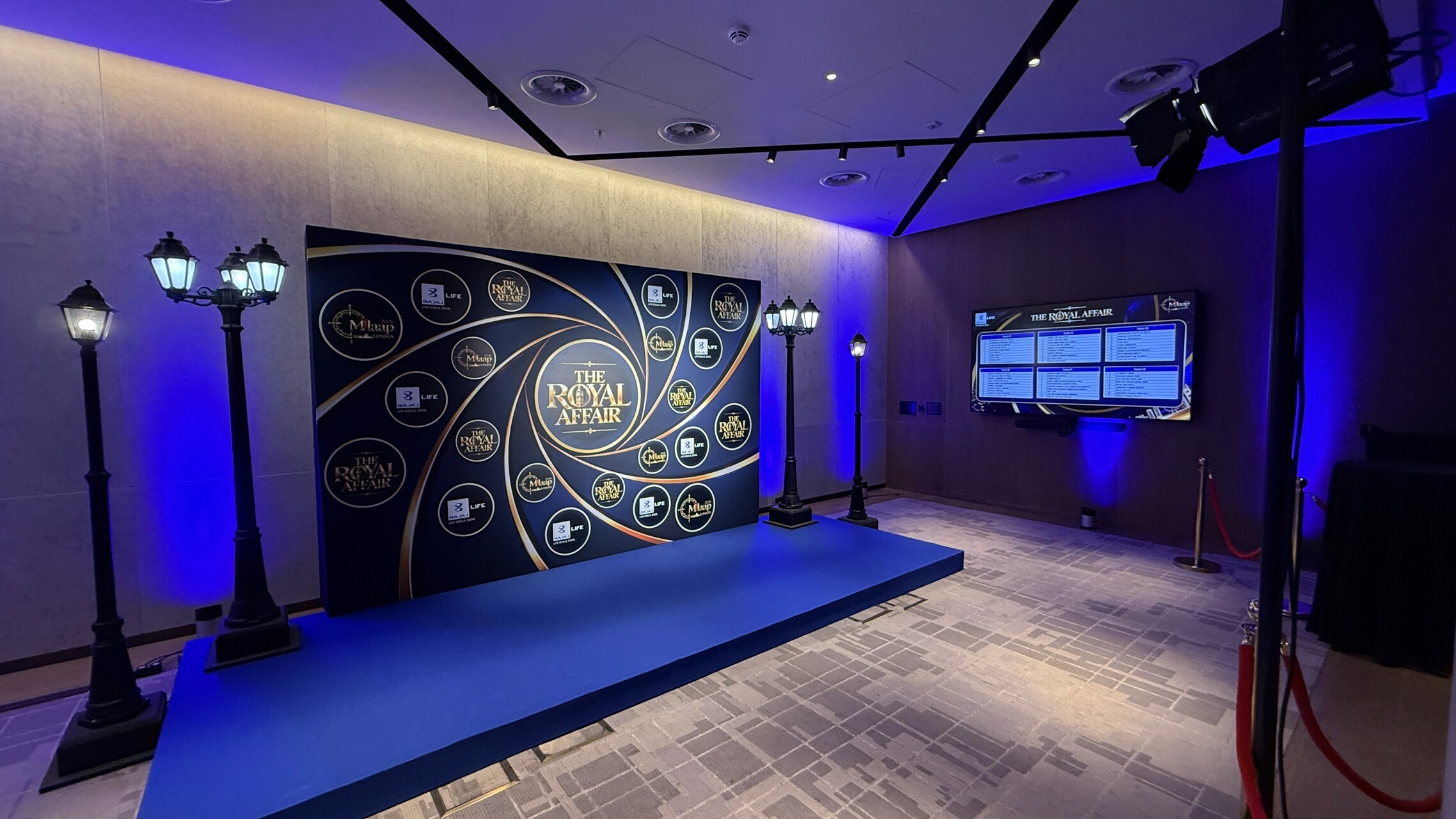 The Royal Affair branded photo backdrop on a blue-carpeted riser, framed by decorative street lamps and blue uplighting.