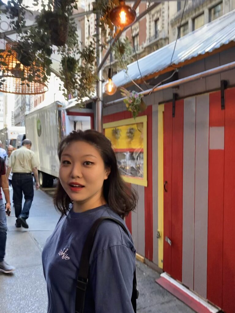 girl with brown hair in front of red building