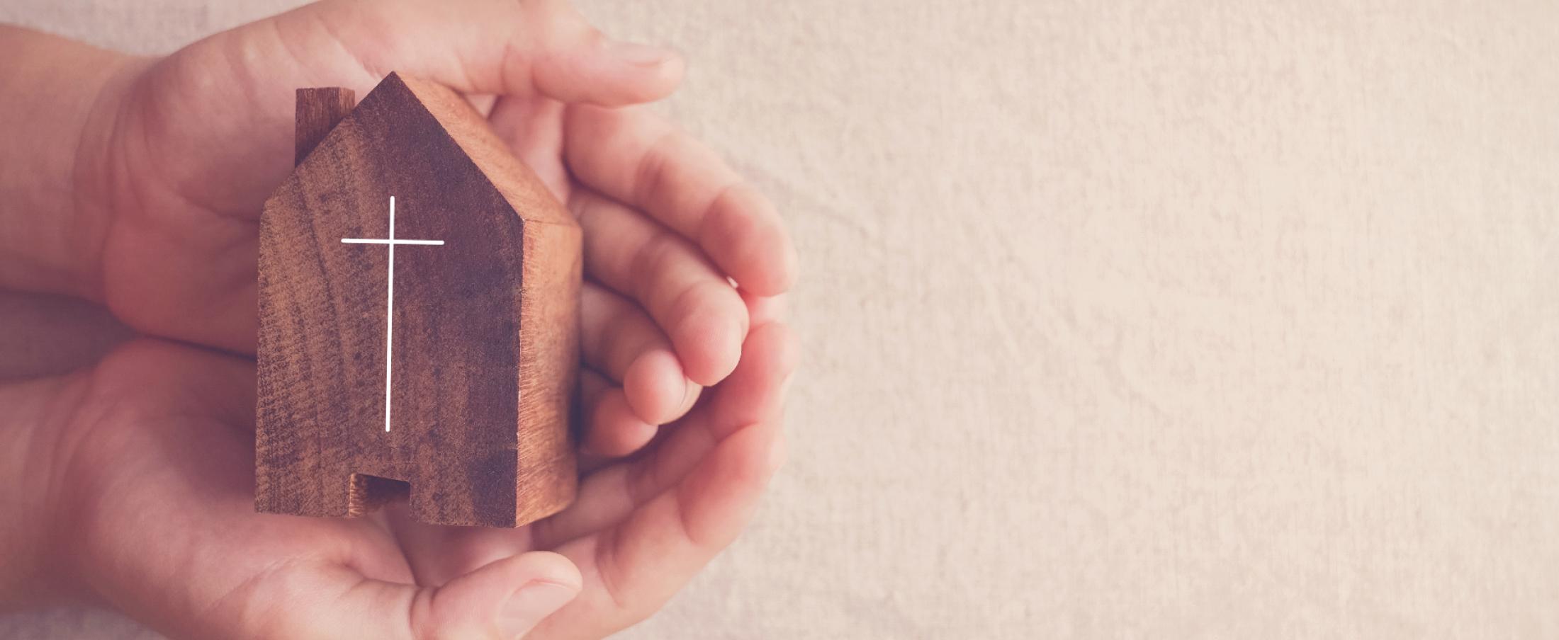 Manos sosteniendo una figura tallada de iglesia con cruz – categoría Teología