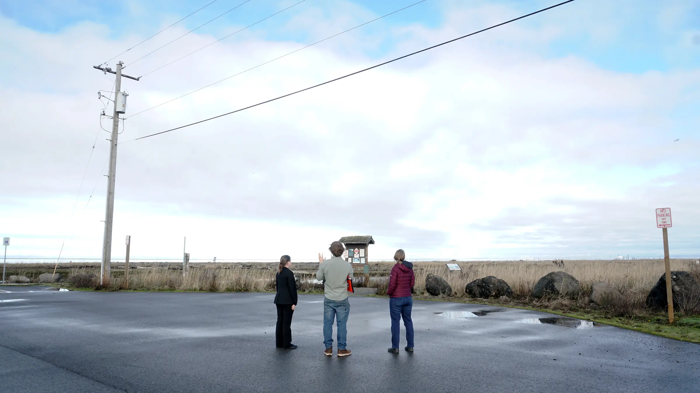 Lara and Phebe from the Collaborative talking with Alex from Jamestown S'Klallam Tribe with their backs to the camera. They are looking at a coastal community in Clallam County, where coastal flooding is a common occurance.