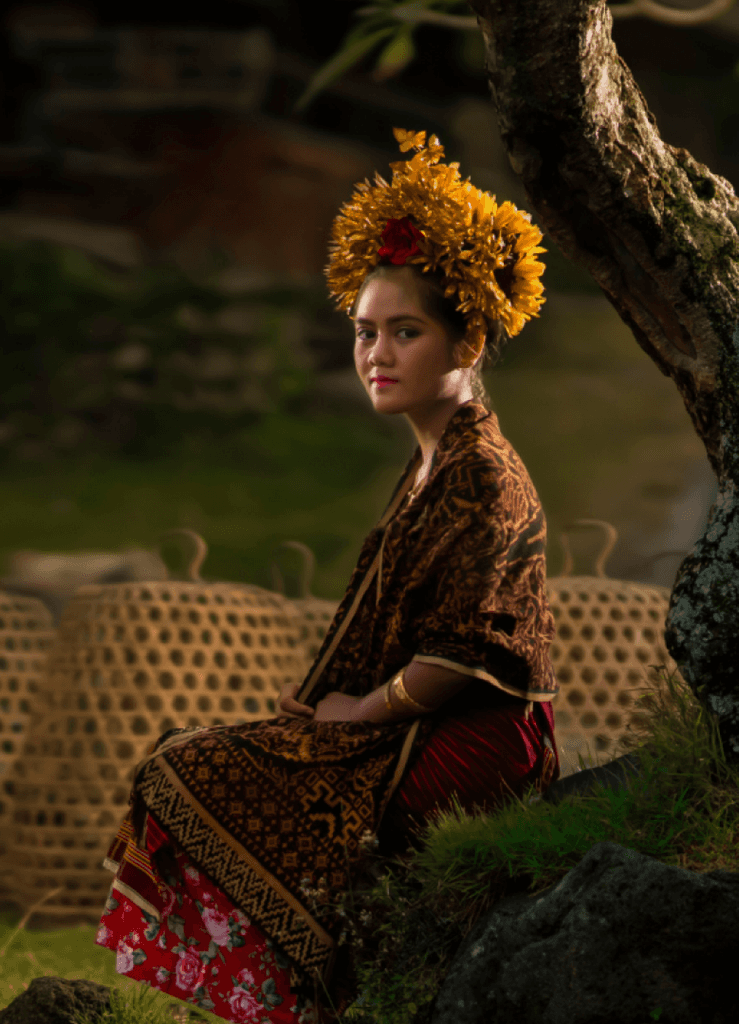 A smiling young man with crossed arms, wearing a plaid shirt and white t-shirt, poses against a dark background.