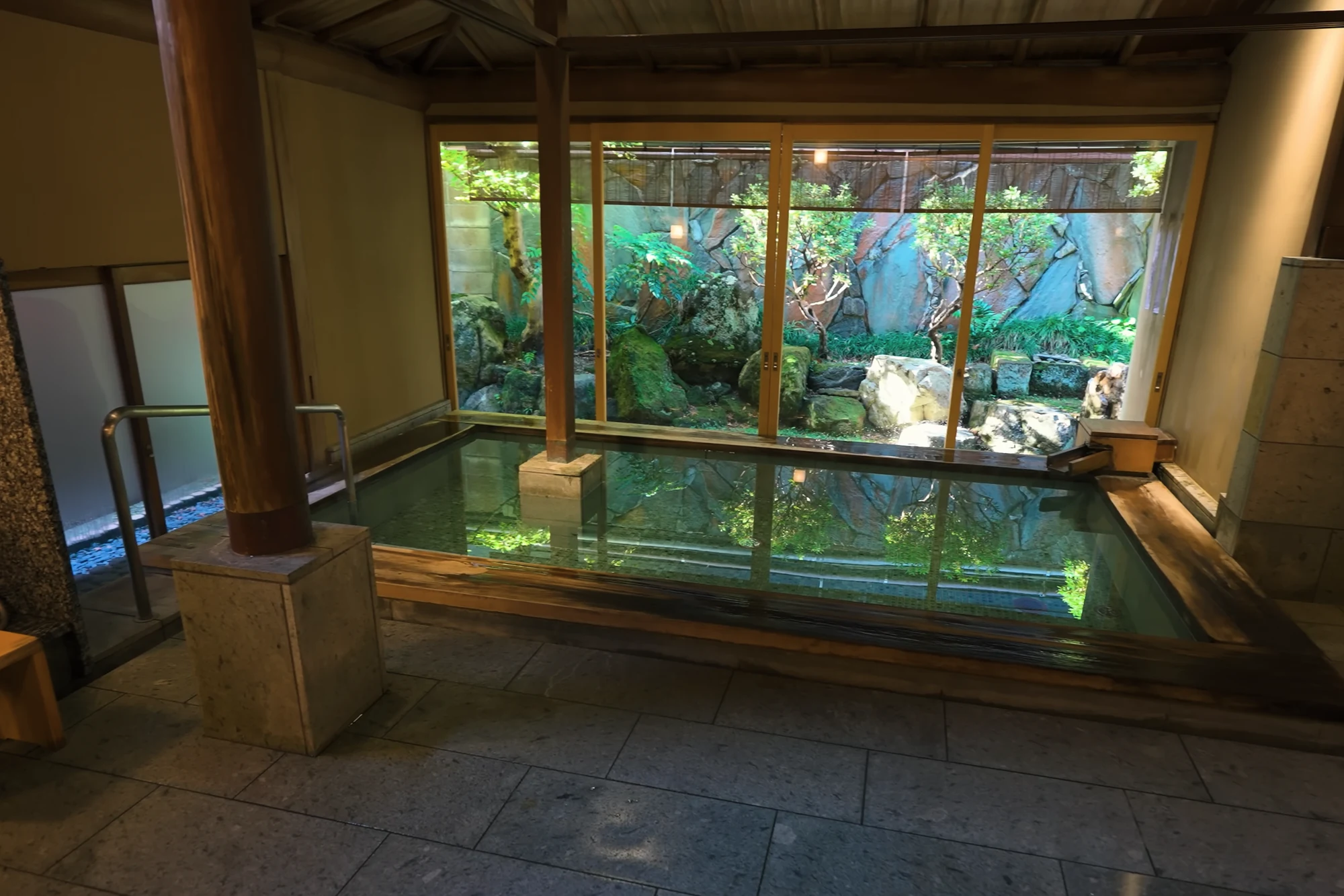 A stone-floored public bath in Kinosaki with a garden behind full-height glass.