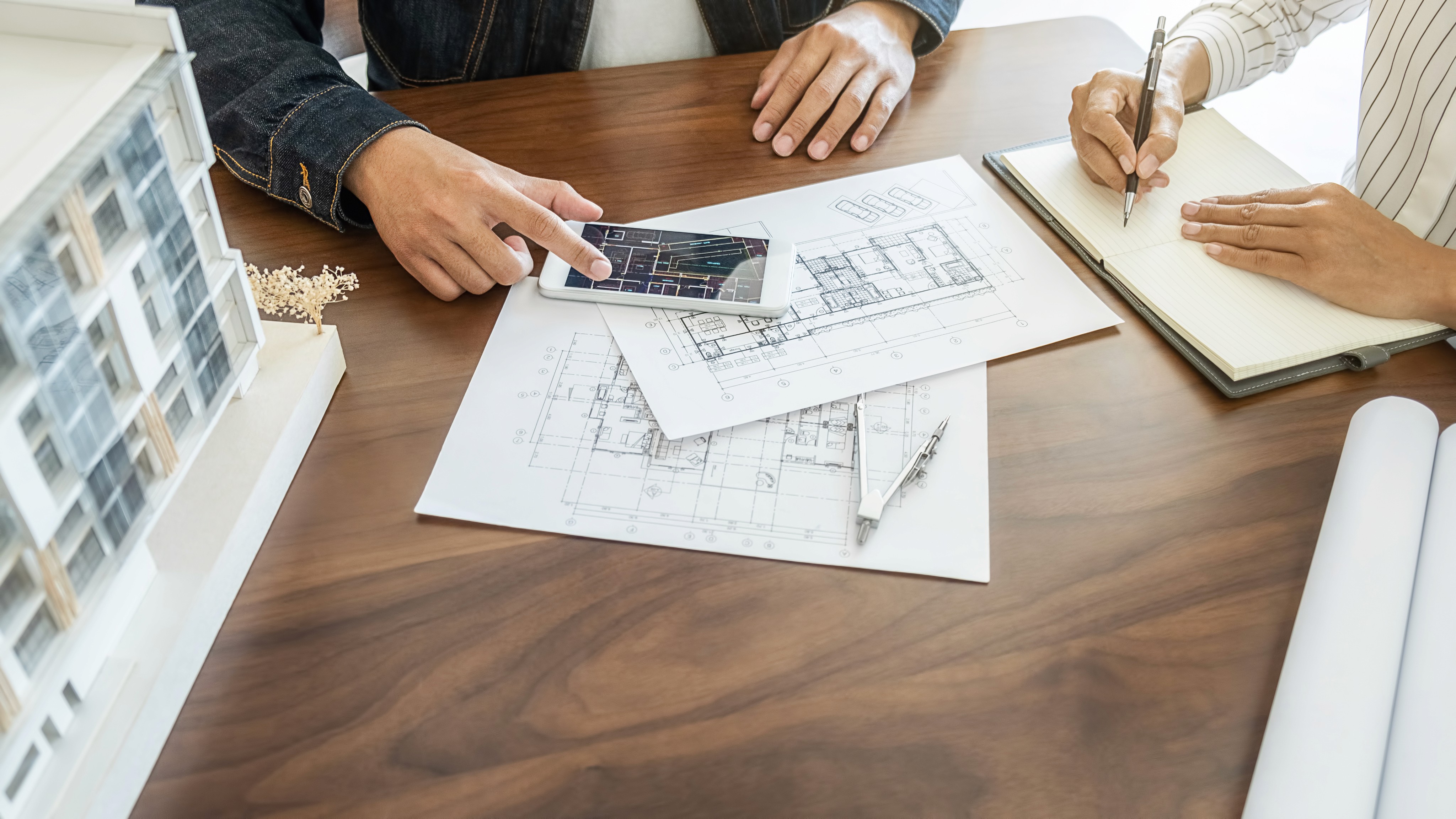 Close-up of architects using pencils to draft detailed technical site plans and urban layouts on large paper.