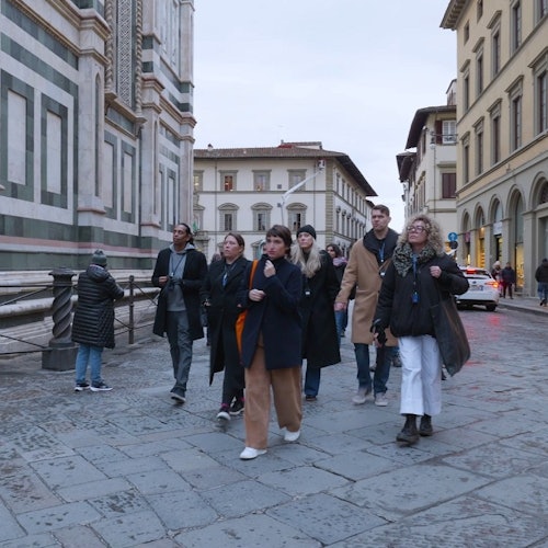 Група людей, які йдуть разом брукованою вулицею поруч з історичною будівлею в європейському місті.