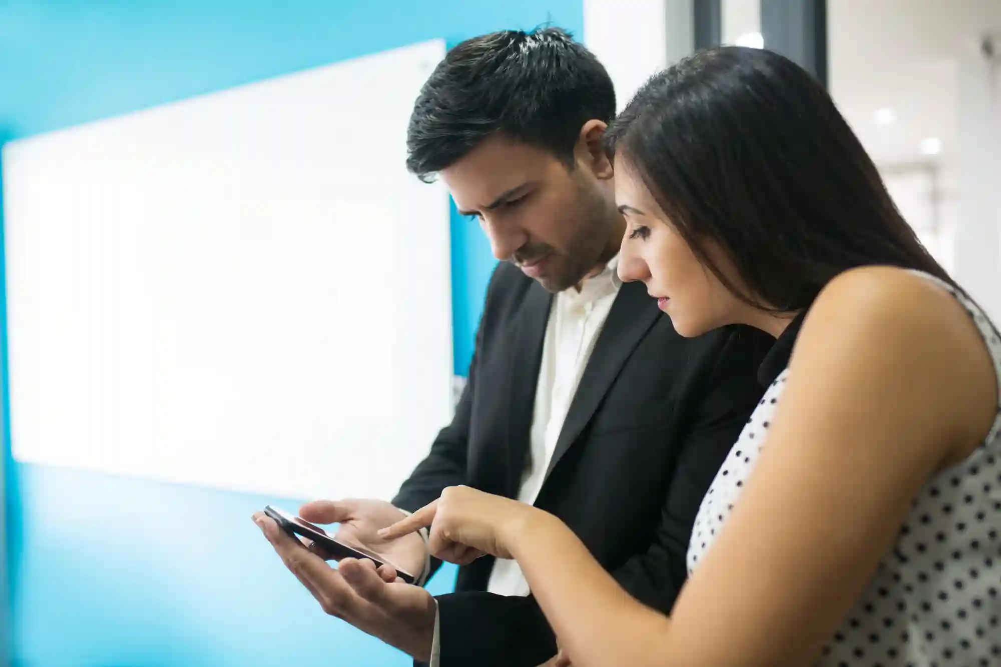 Two professionals collaborate by reviewing data on a smartphone to make quick, informed decisions in a corporate hallway.