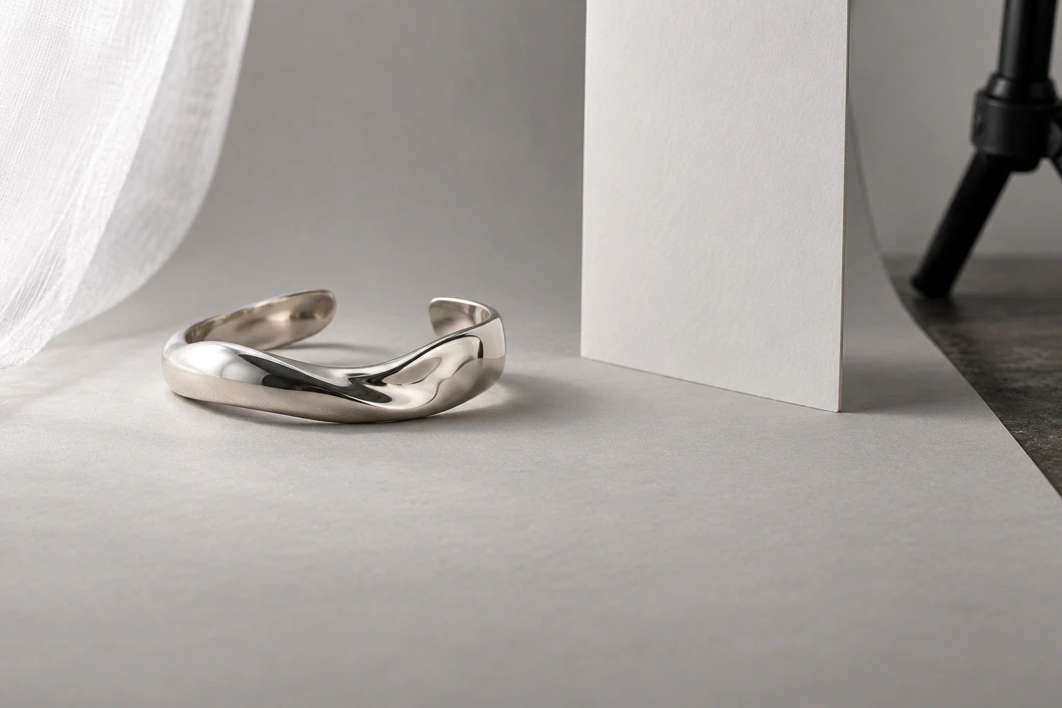 Silver cuff beside an upright white card with a diffuser and tripod leg at the edges
