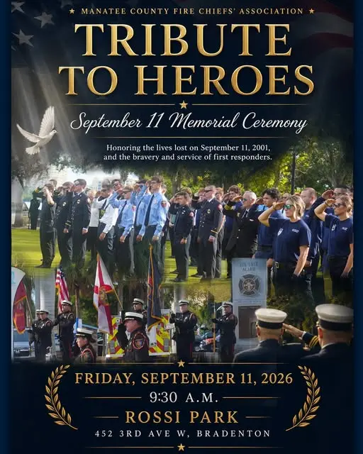 A group of uniformed individuals stands solemnly under flags, commemorating the bravery and service of first responders at the "Tribute to Heroes" September 11 Memorial Ceremony in Rossi Park, Bradenton, FL.