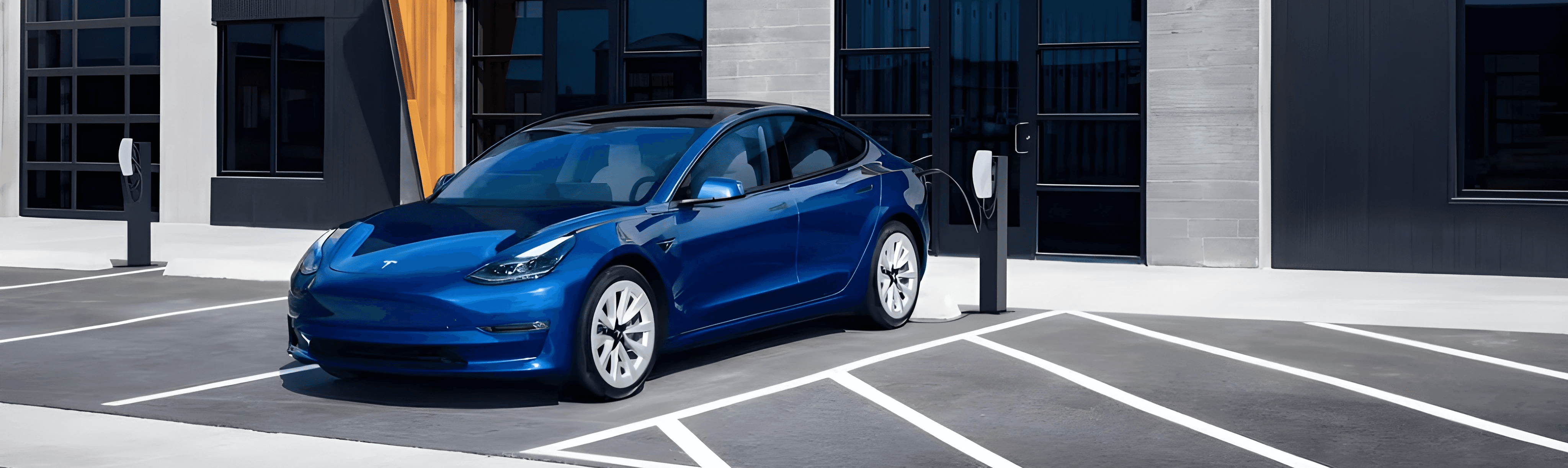 Tesla Model 3 bleue en recharge sur parking, berline électrique devant un immeuble contemporain