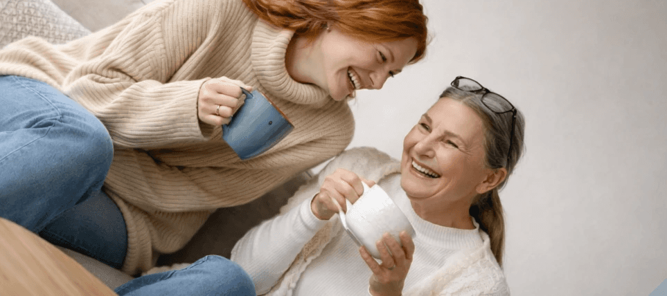 Junge Frau und ältere Frau trinken zusammen Tee und lachen.