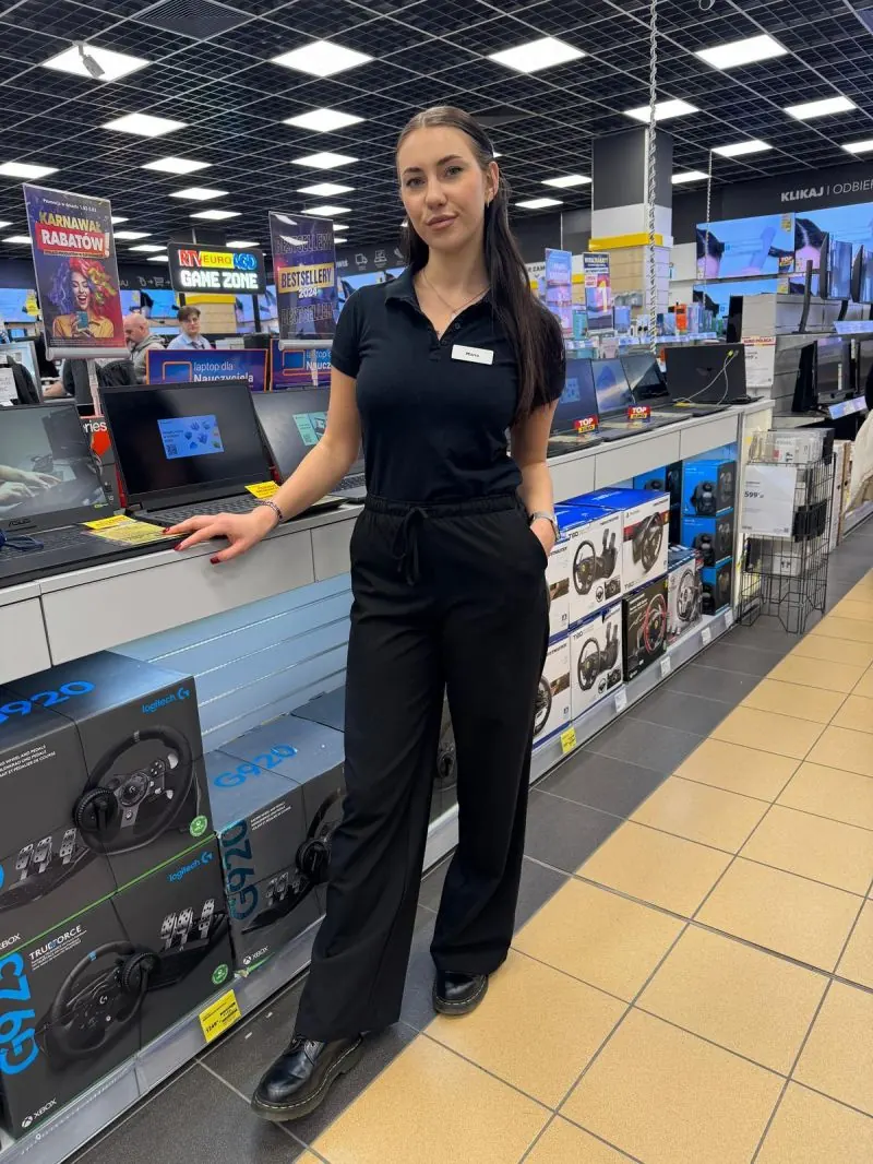 Promotorka Lenovo w czarnej koszulce polo przy ekspozycji sklepowej.