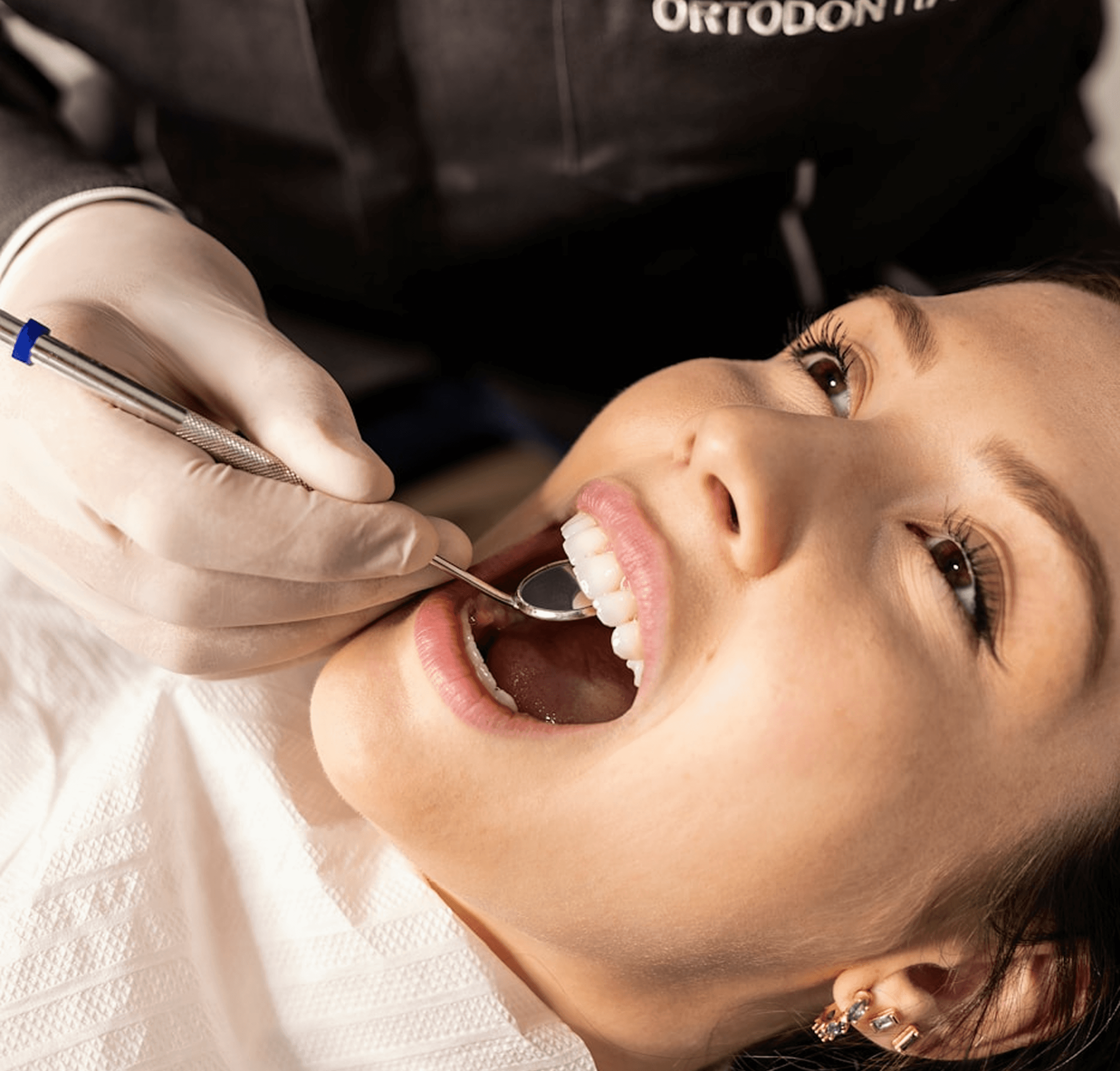 Orthodontist in dark uniform using dental mirror to examine patient’s teeth during check-up