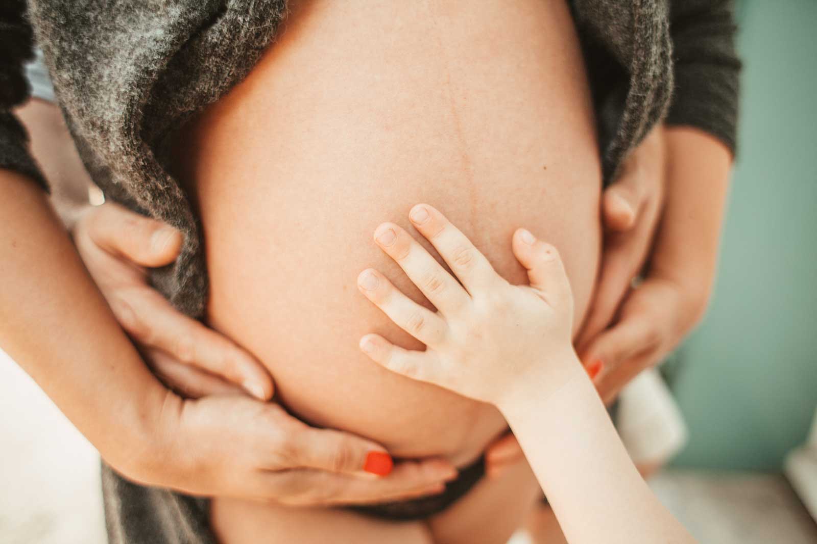 verschiedene Hände berühren den Bauch einer schwangeren Frau