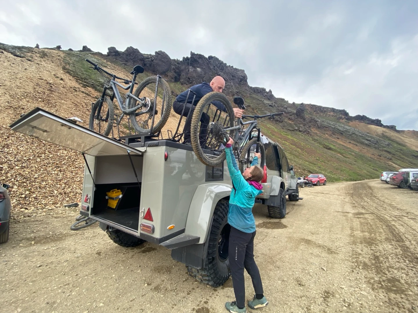 A man stands on biketrailer and hands a woman a bike in Landmannalaugar