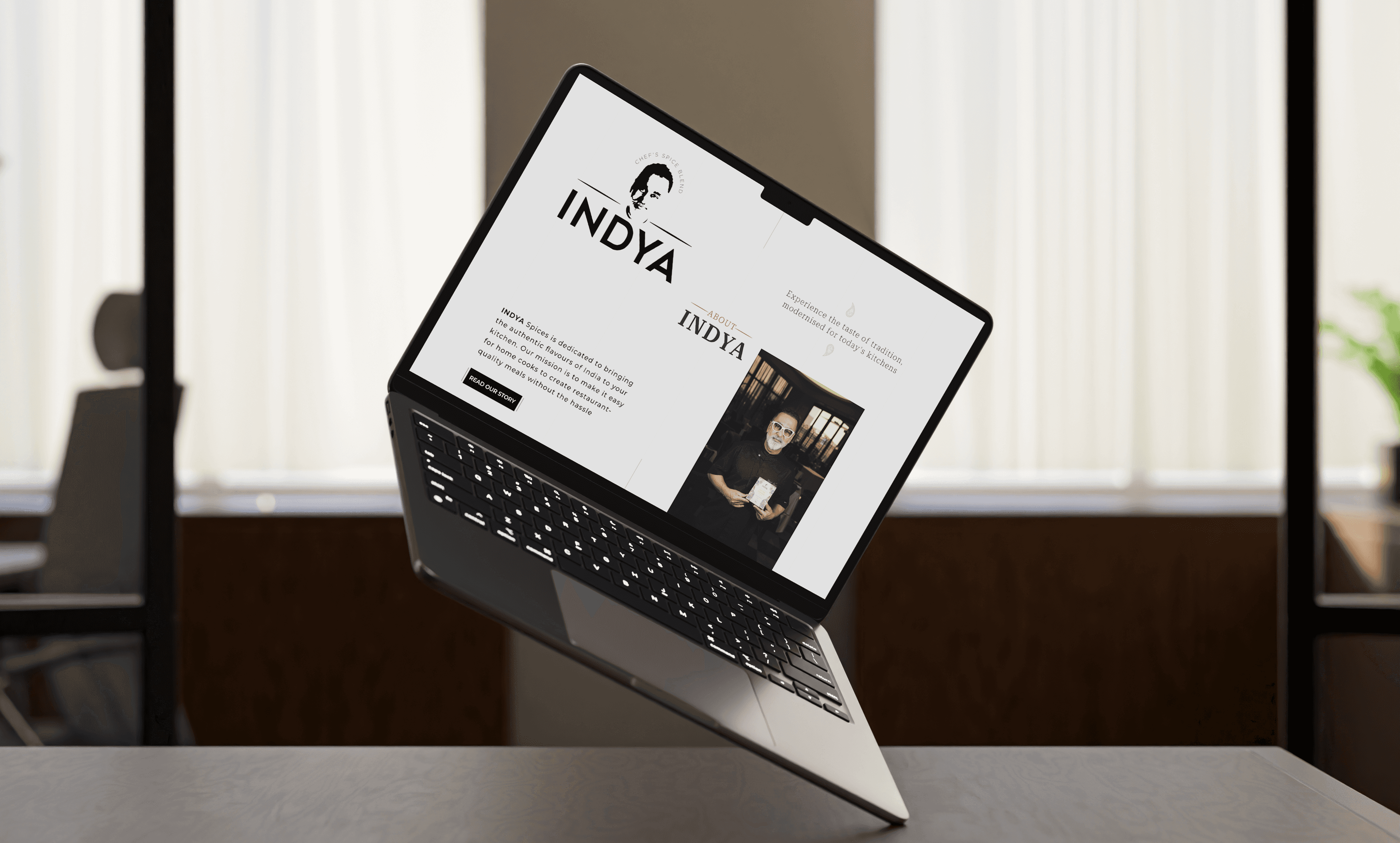 Open laptop displaying the INYA Spices website with a section about the brand and Chef Vineet Bhatia. The screen features the INYA logo, a brief brand description, and an image of the chef holding a product. The background shows a modern, softly lit office space.