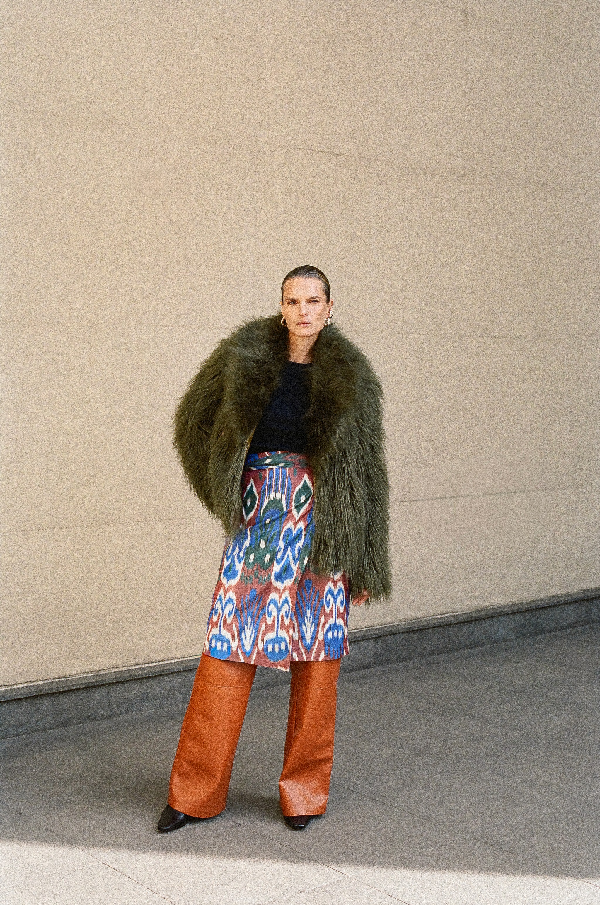 Woman standing in a field wearing a white shirt and long yellow patterned coat, shielding her eyes from the sun.