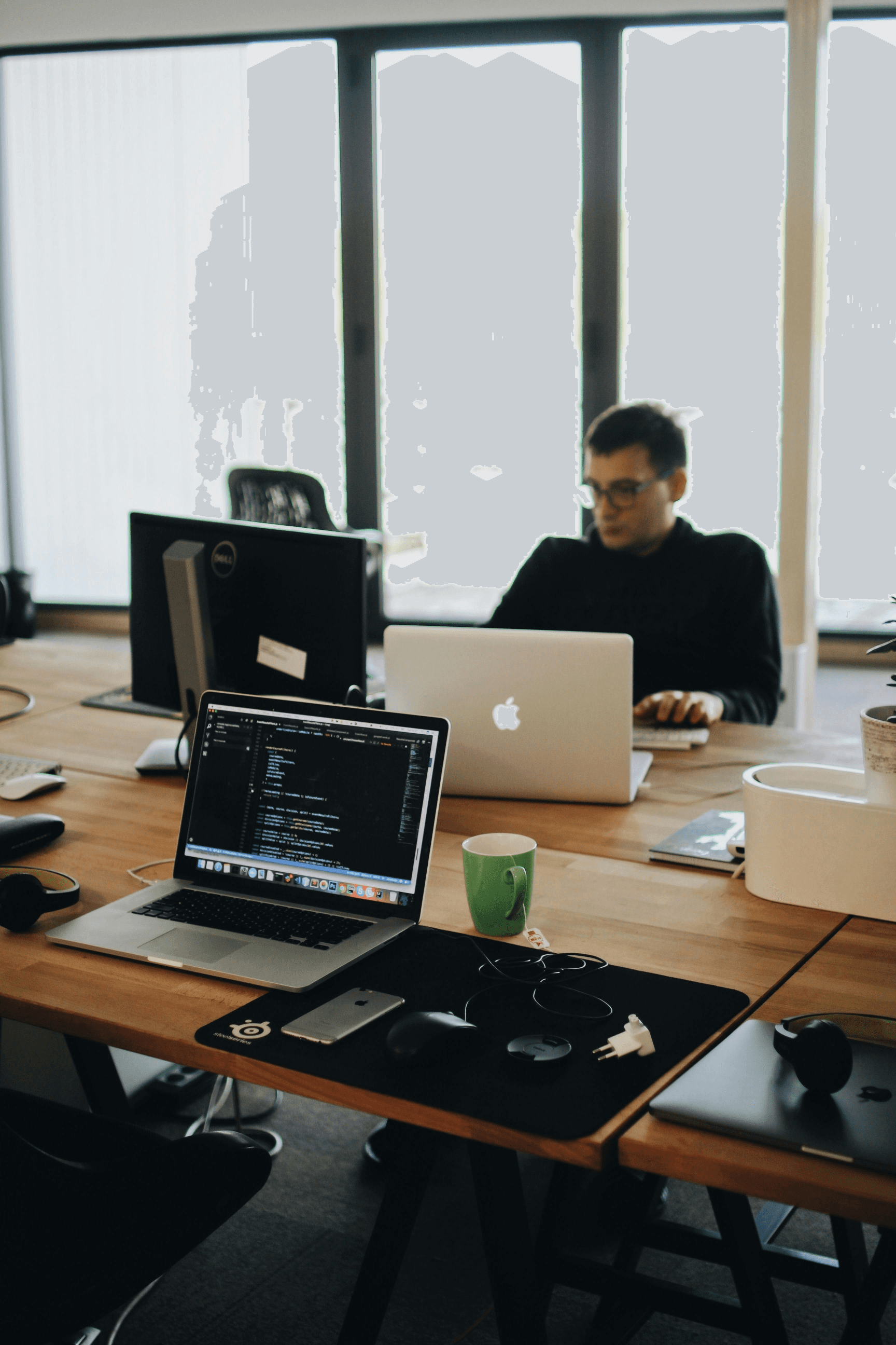 Modern office workspace with laptops, coding on screen, developer at desk.