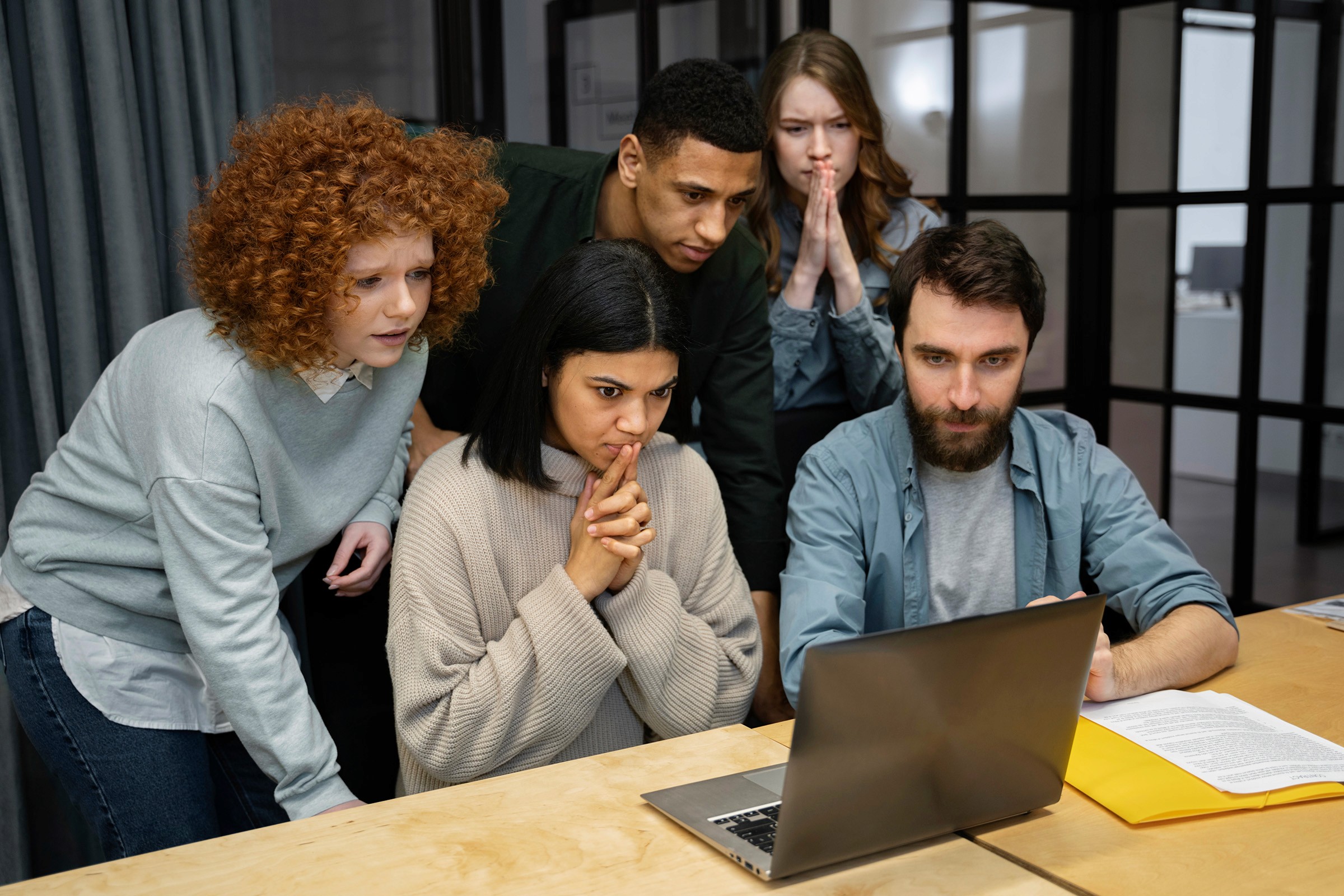 A group of focused colleagues gathered around a laptop, deeply engaged in a discussion or presentation