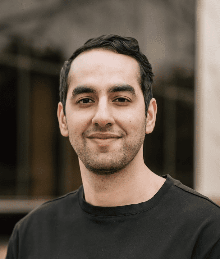 A woman with short curly hair wearing a black t-shirt looks into the camera.