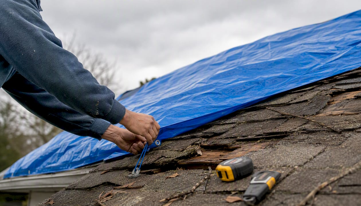 Roofer installing temporary tarp on roof damage
