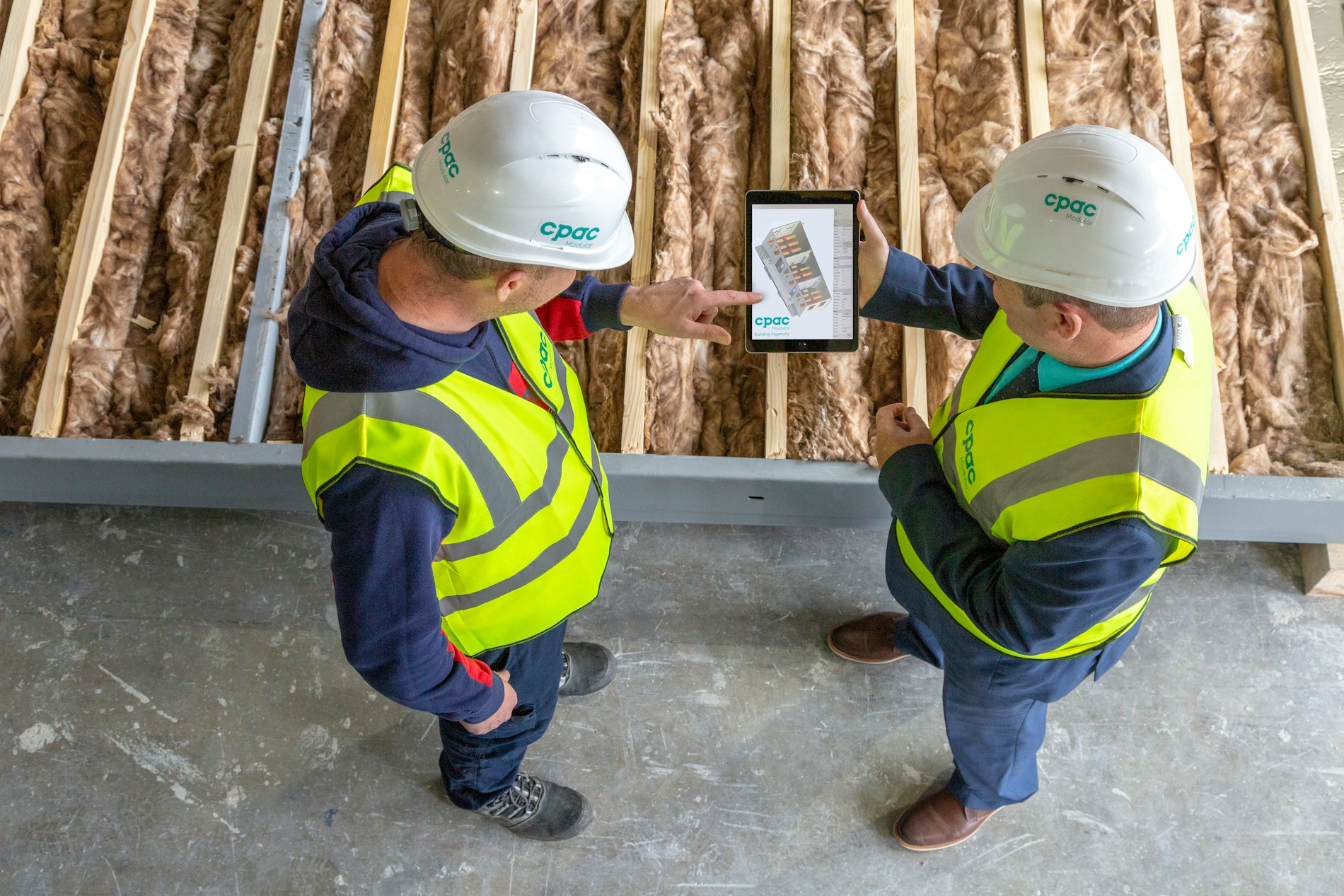 Two construction workers reviewing plans on a digital tablet on site